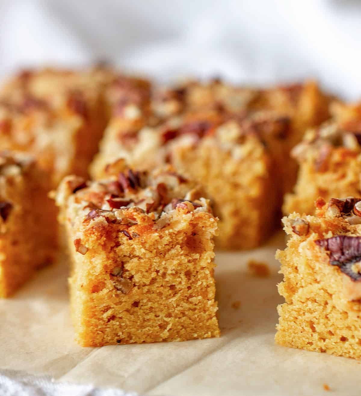 Small squares of pecan topped pumpkin cake on beige parchment paper with grey background.