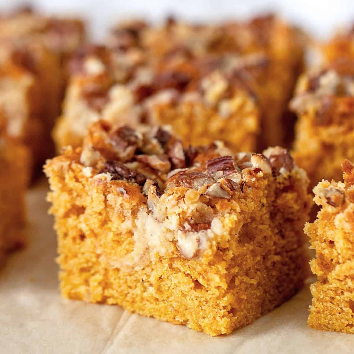 One main square of pecan topped pumpkin cake, others blurred on a grey background.