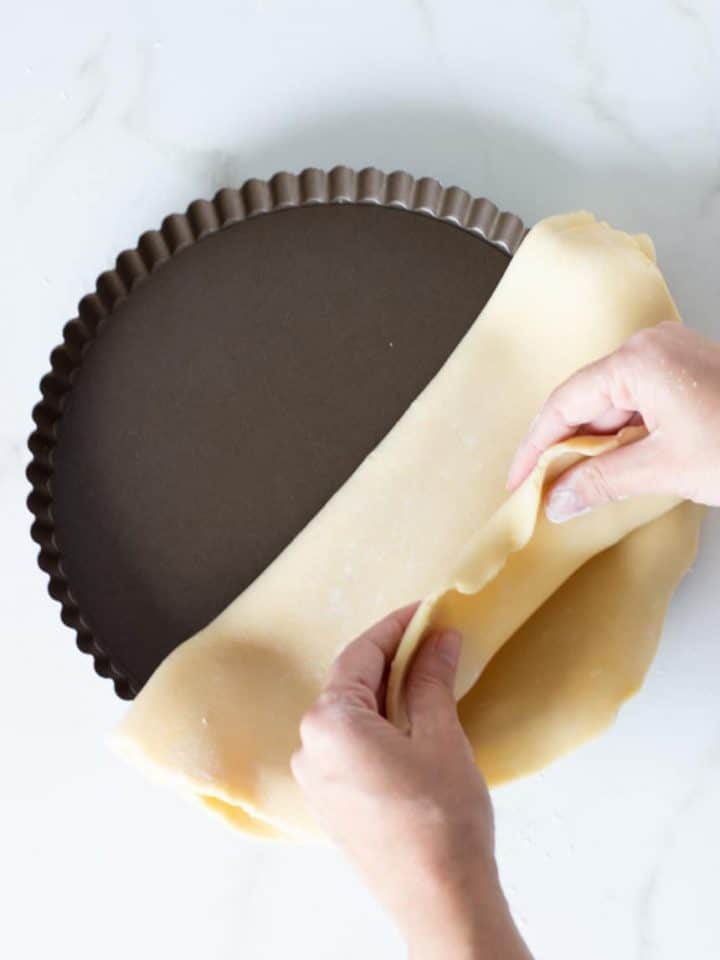 Hands lining pie pan with Unbaked sweet shortcrust pastry