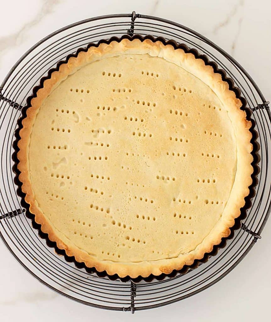 Round tart pan with baked homemade pie crust on wire rack