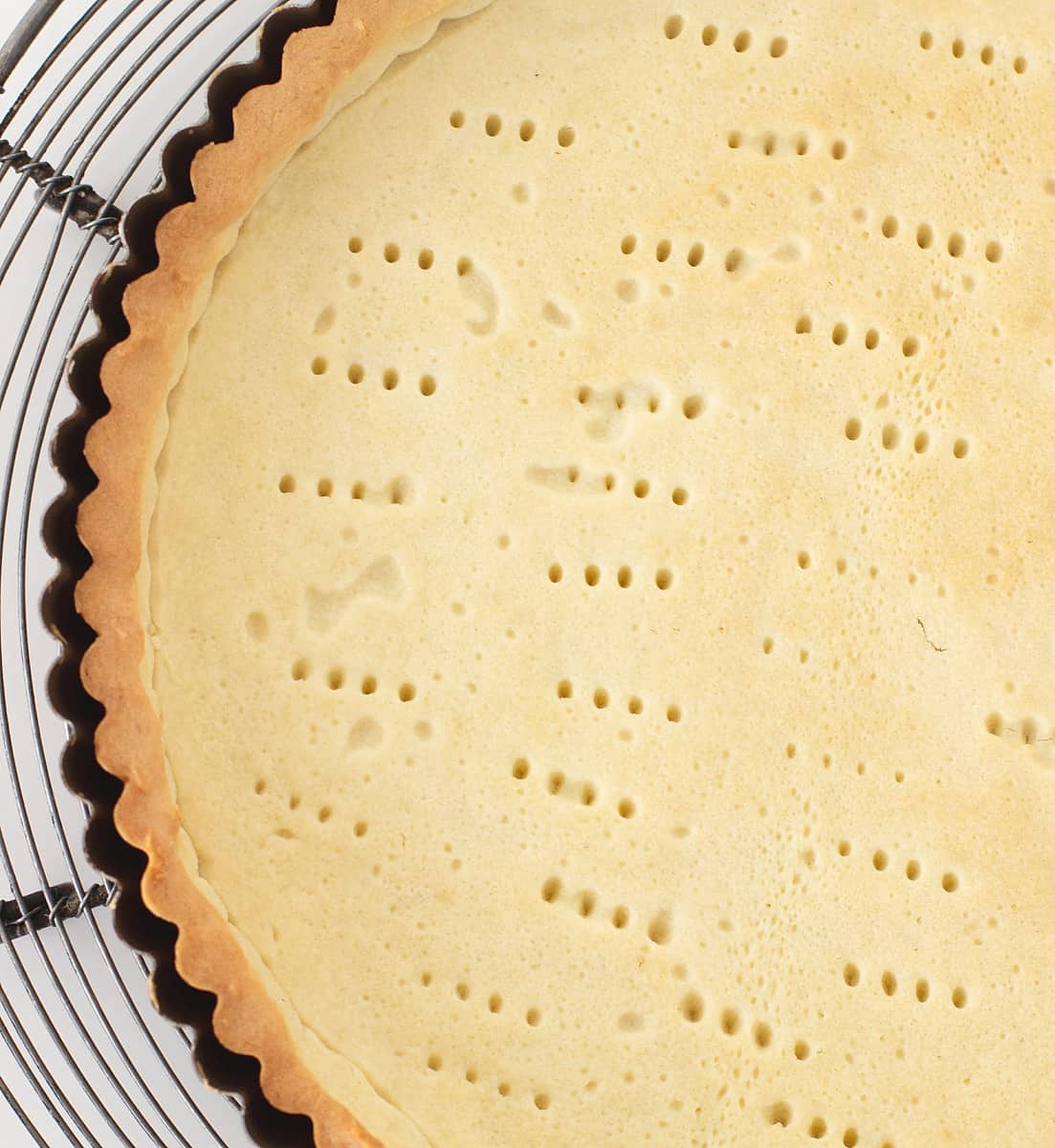 Partial overview of baked tart dough in pan on wire rack