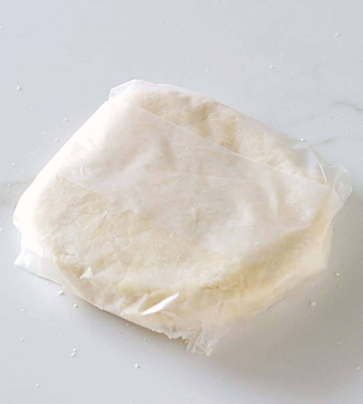Disc of pie crust wrapped in plastic on white surface