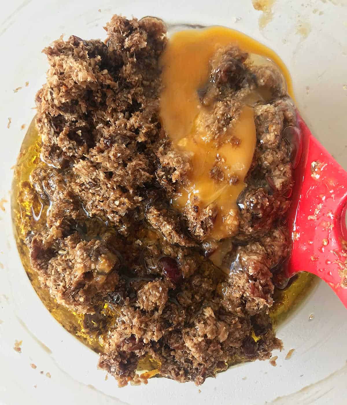 Egg added to raisin bran muffin batter in a bowl with a red spatula.