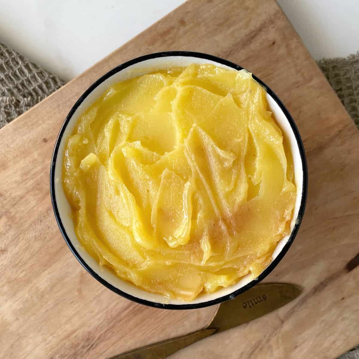 Brown butter in a black rimmed white bowl on a wooden board.