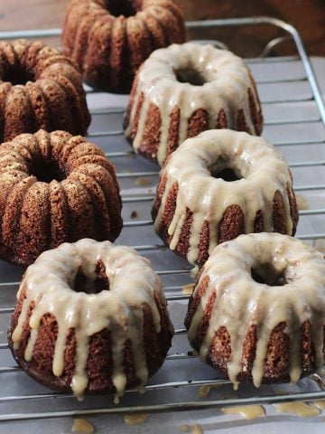 Two rows of glazed mini chocolate cakes on a wire rack with parchment underneath.