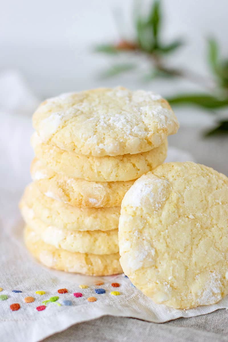 Stack of lemon crinkle cookies, white cloth with color dots, green leaves in background