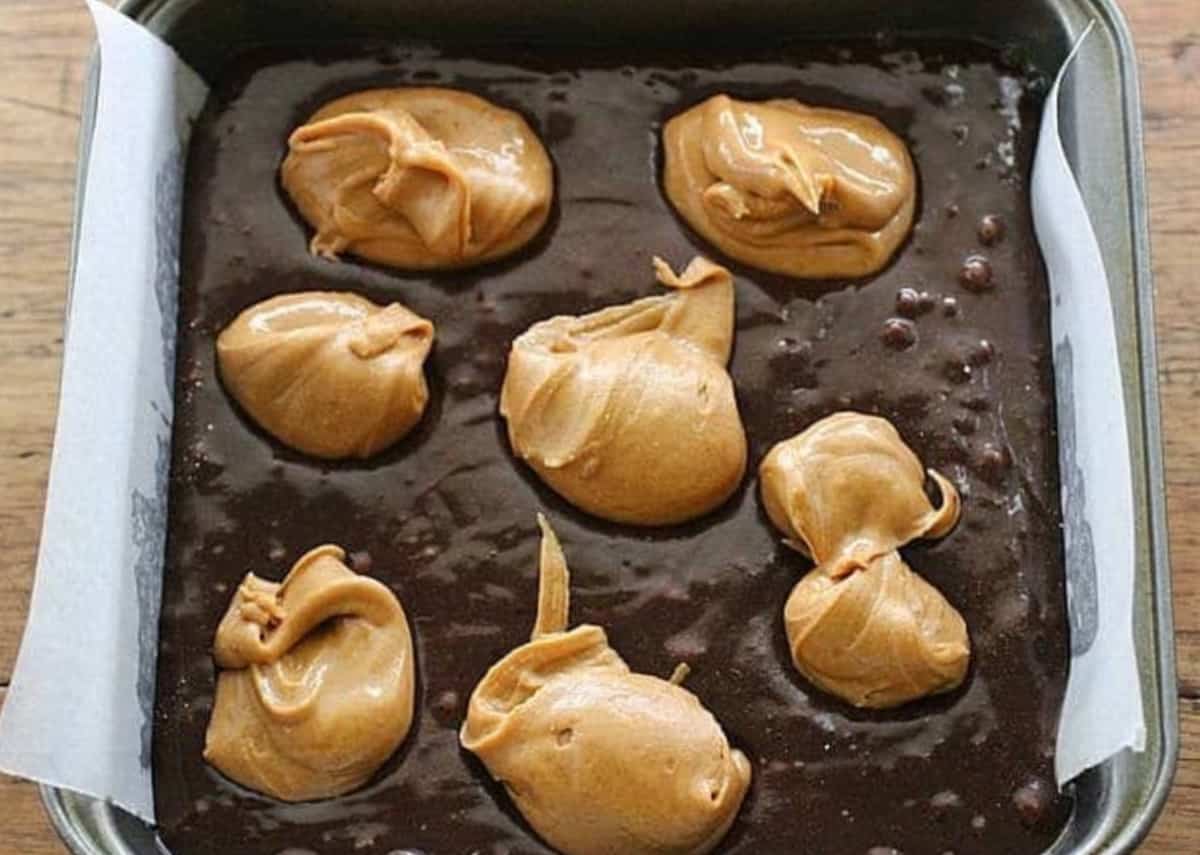 Brownie batter in metal pan, peanut butter mounds on top