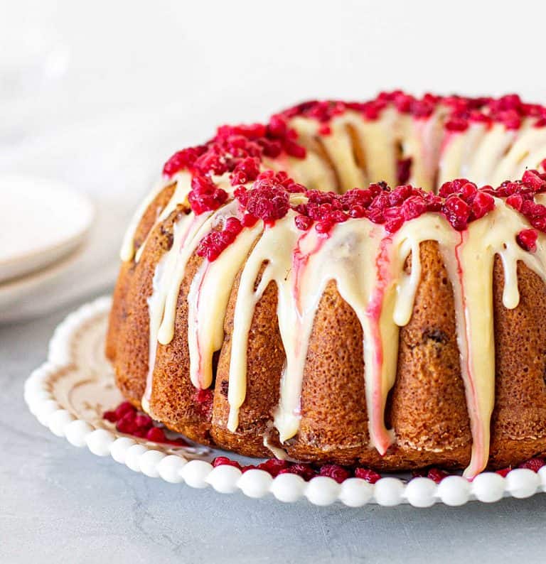 Glazed white chocolate raspberry bundt cake on white plate, grey background