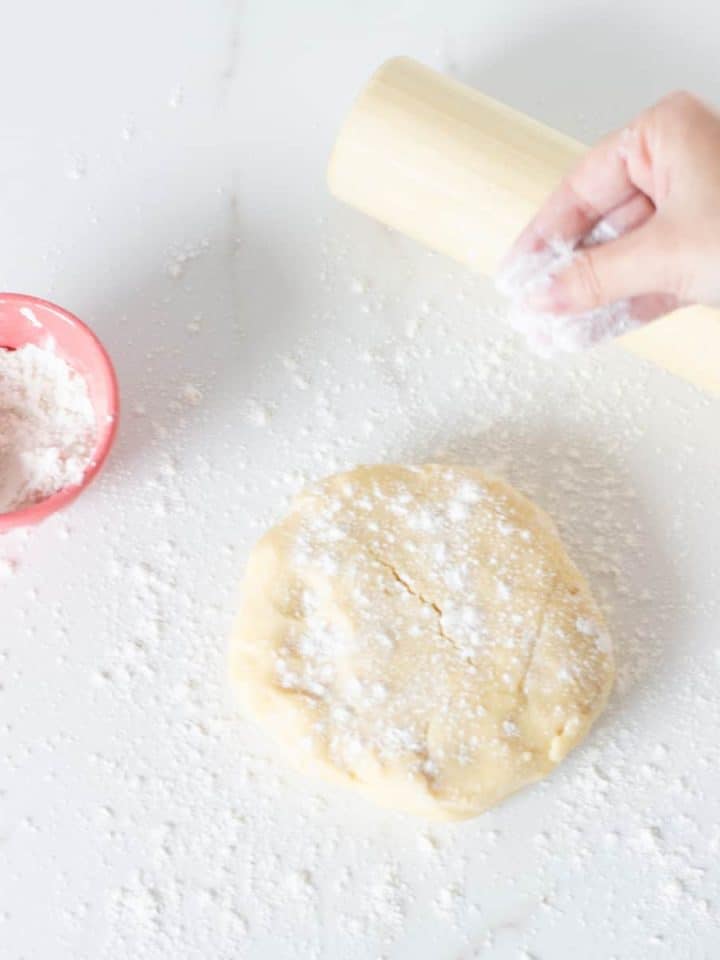 Hand flouring basic pie dough on white surface, rolling pin, pink bowl