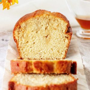 Close up image of cut loaf cake with slices on white paper on a white surface.