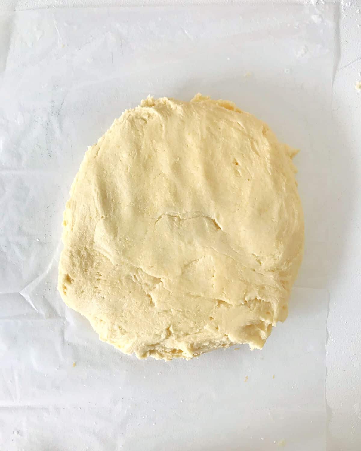 Round disc of vanilla dough on a transparent sheet of paper on a white surface.