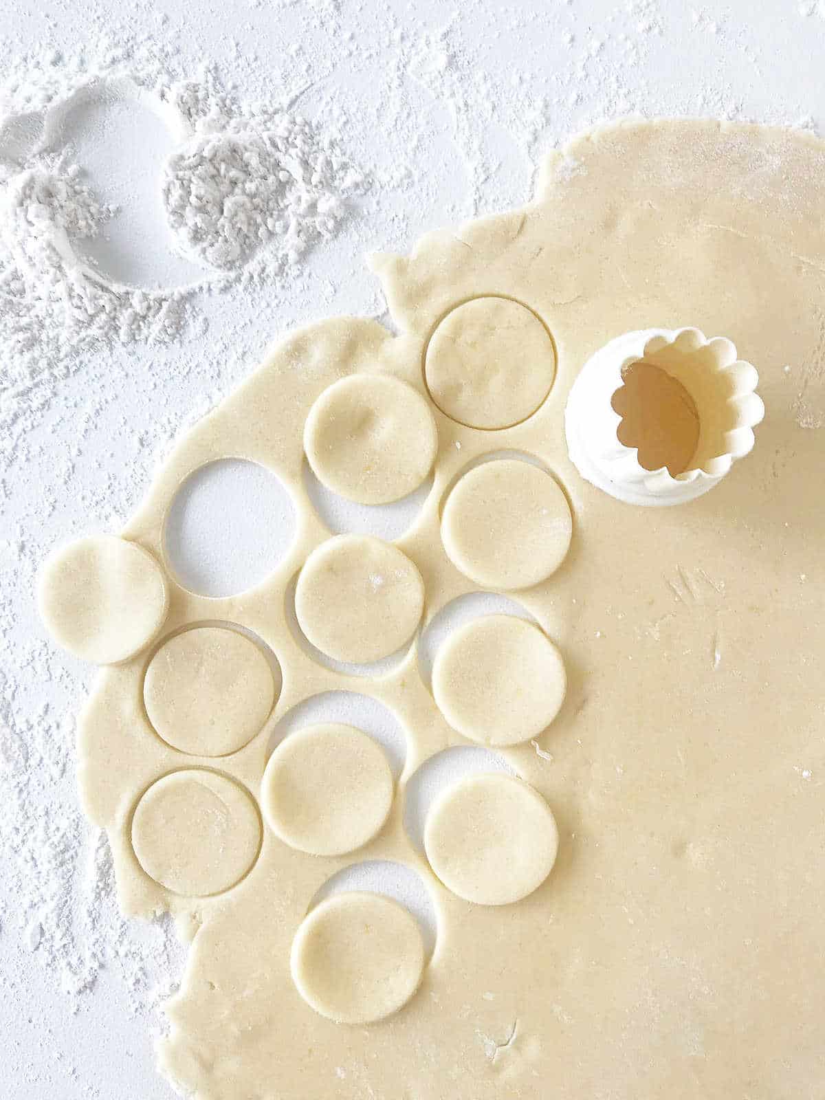 Rolled cookie dough on a floured white surface with round cutter and some cut circles of dough.