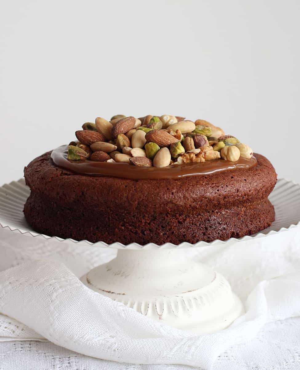 Nut topped Chocolate cake on white cake stand, white background.