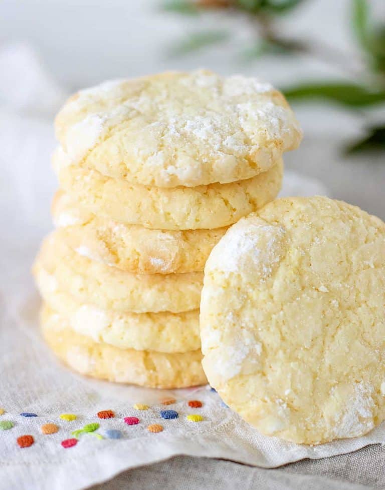 Stack of lemon crinkle cookies, white cloth with color dots, green leaves in background