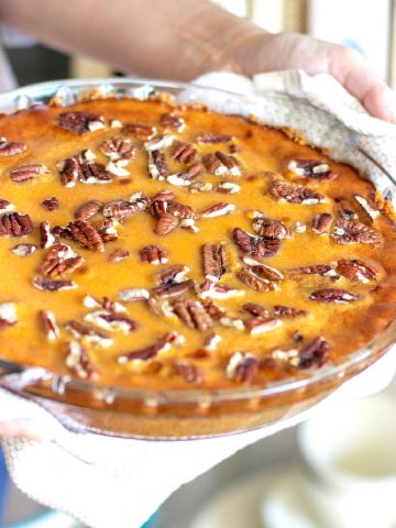 On a white plate and surface, an eaten slice of sweet potato pie with pecans, a silver fork