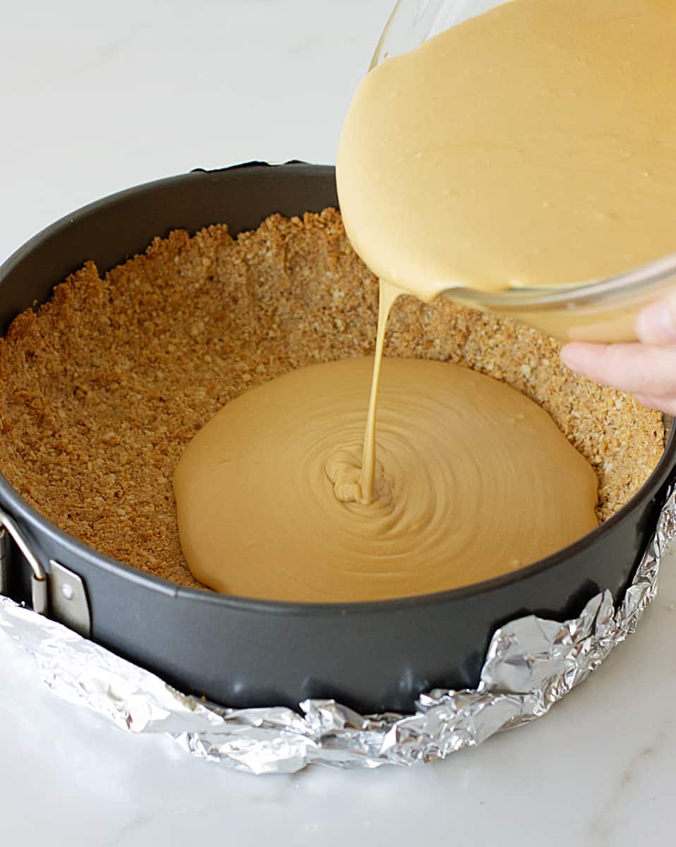 Pouring cheesecake filling into cookie crust in round pan