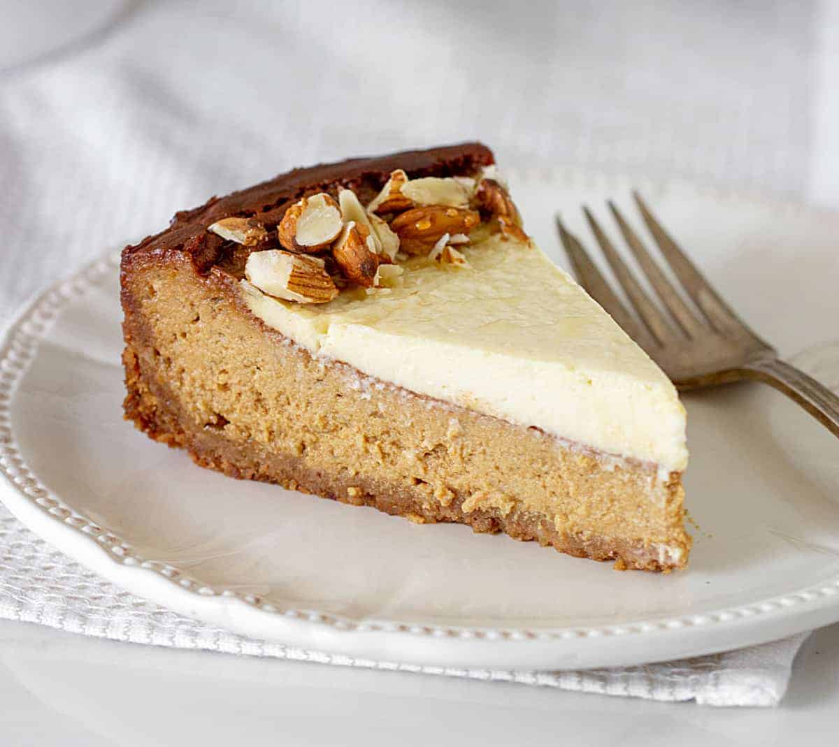 Slice of brown sugar cheesecake on a white plate with a silver fork. White surface.