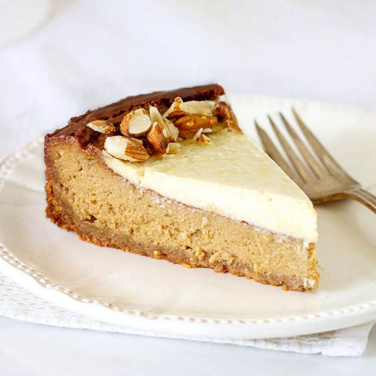 Single slice of brown sugar cheesecake with sour cream topping on a white plate. Silver fork and white background.