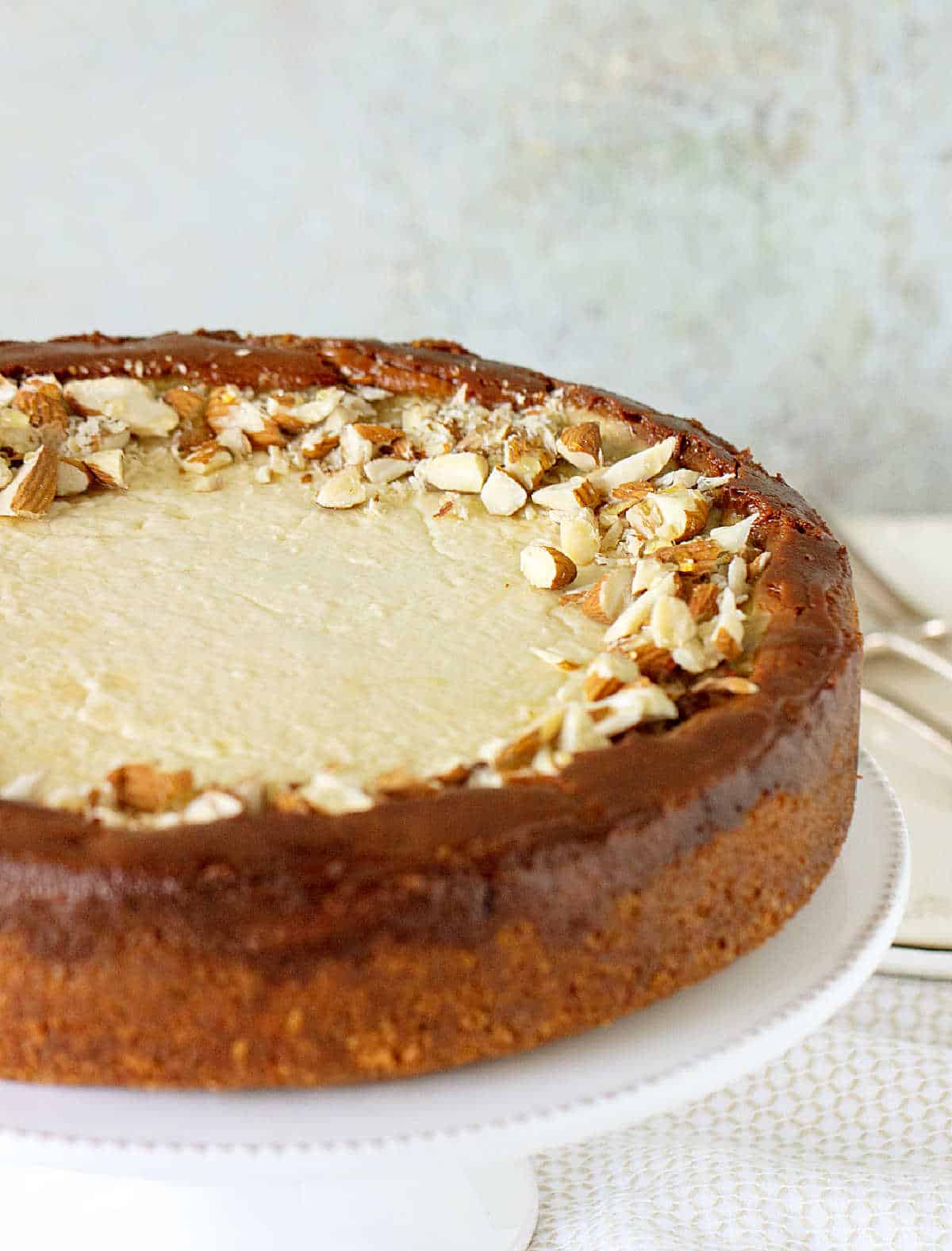 Partial image of whole brown sugar cheesecake on white cake stand. Grey background. 