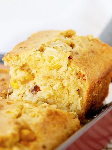 Lifting a square of cheese cornbread from a baking tray.