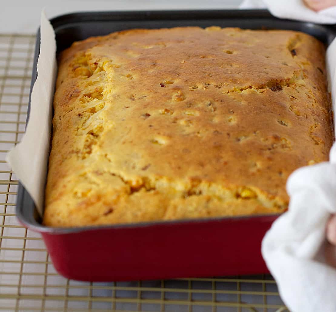 Hands placing baked cornbread in red pan on a wire rack