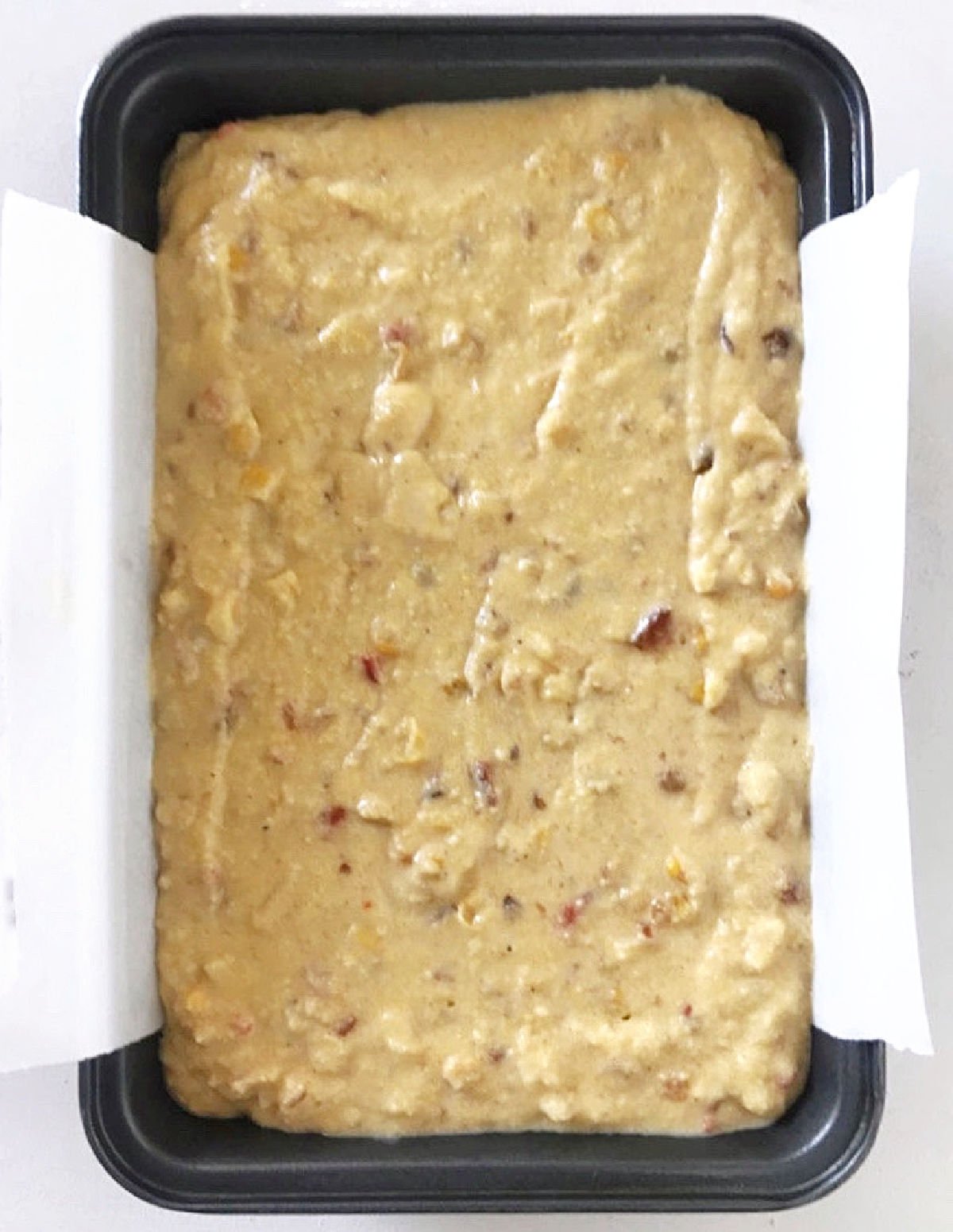 Cornbread batter in a rectangular dark metal pan with parchment paper on a white surface.