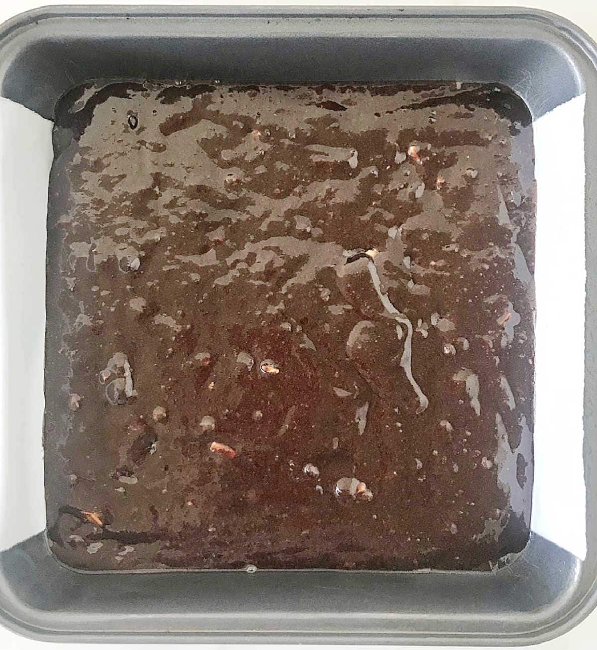 Unbaked brownie batter in metal square pan with parchment paper.