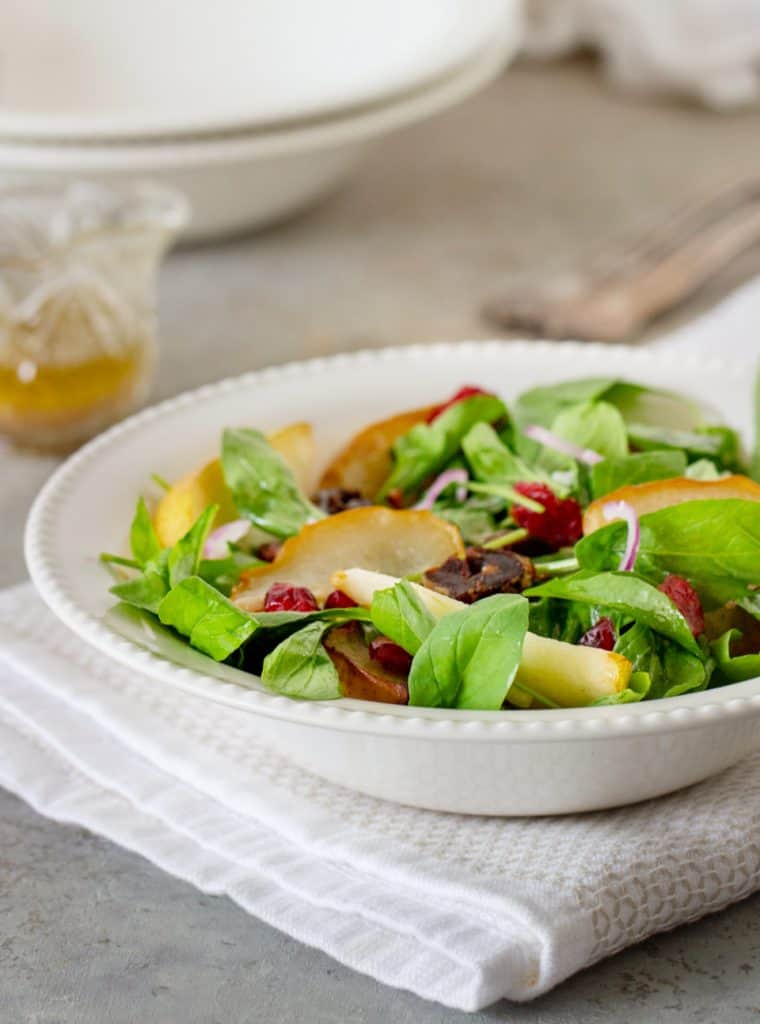 Pear arugula salad on white bowl plate, vinaigrette in jar