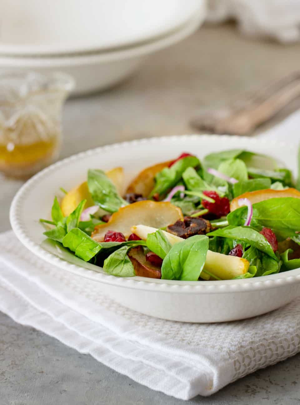 Pear arugula salad on white bowl plate, vinaigrette in jar.