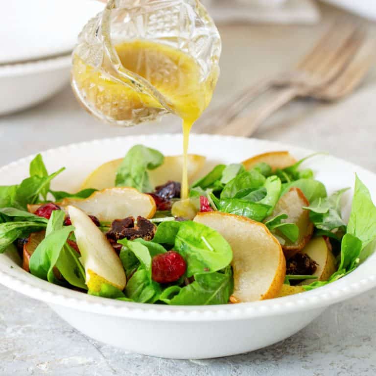 Close up of white plate with arugula pear salad being dressed with vinaigrette in a jar.