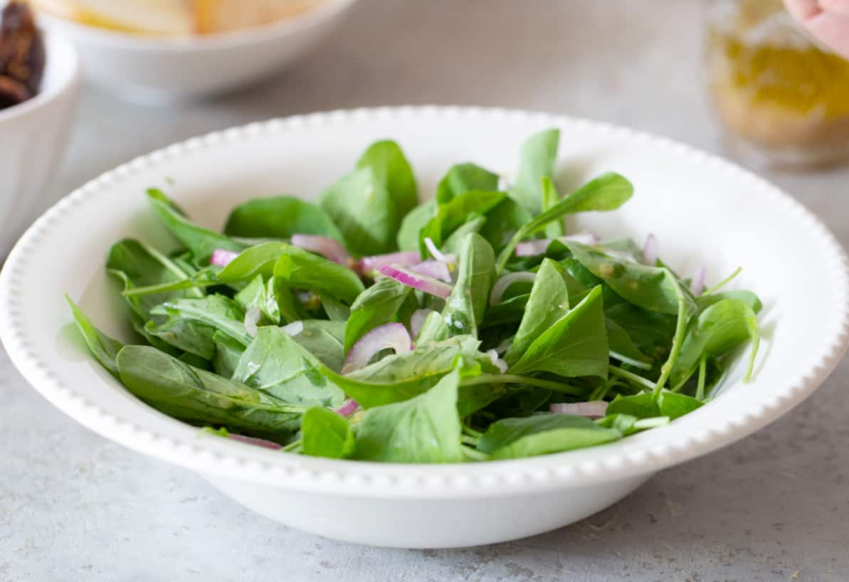 Arugula and onion in white bowl plate, grey surface.