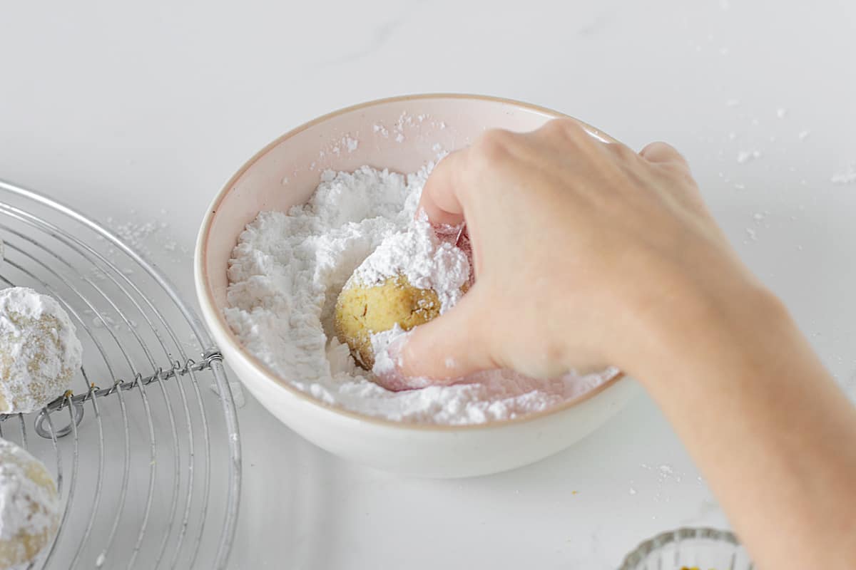 Hand rolling cookie in pink bowl with powdered sugar