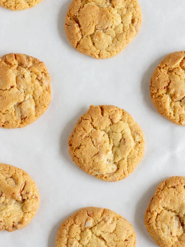 Flat close up view of baked almond cookies on white parchment paper.