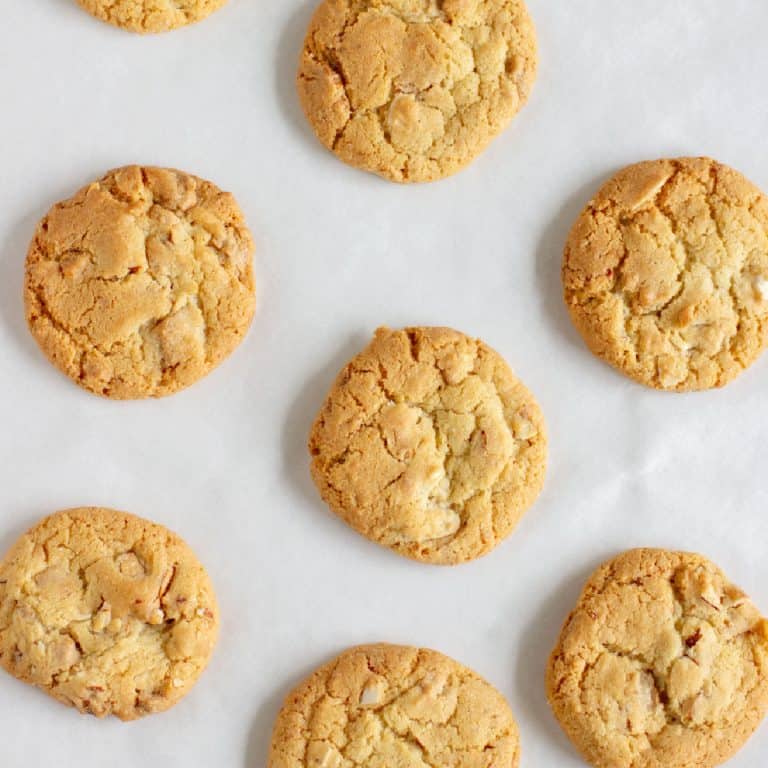 Flat close up view of baked almond cookies on white parchment paper.