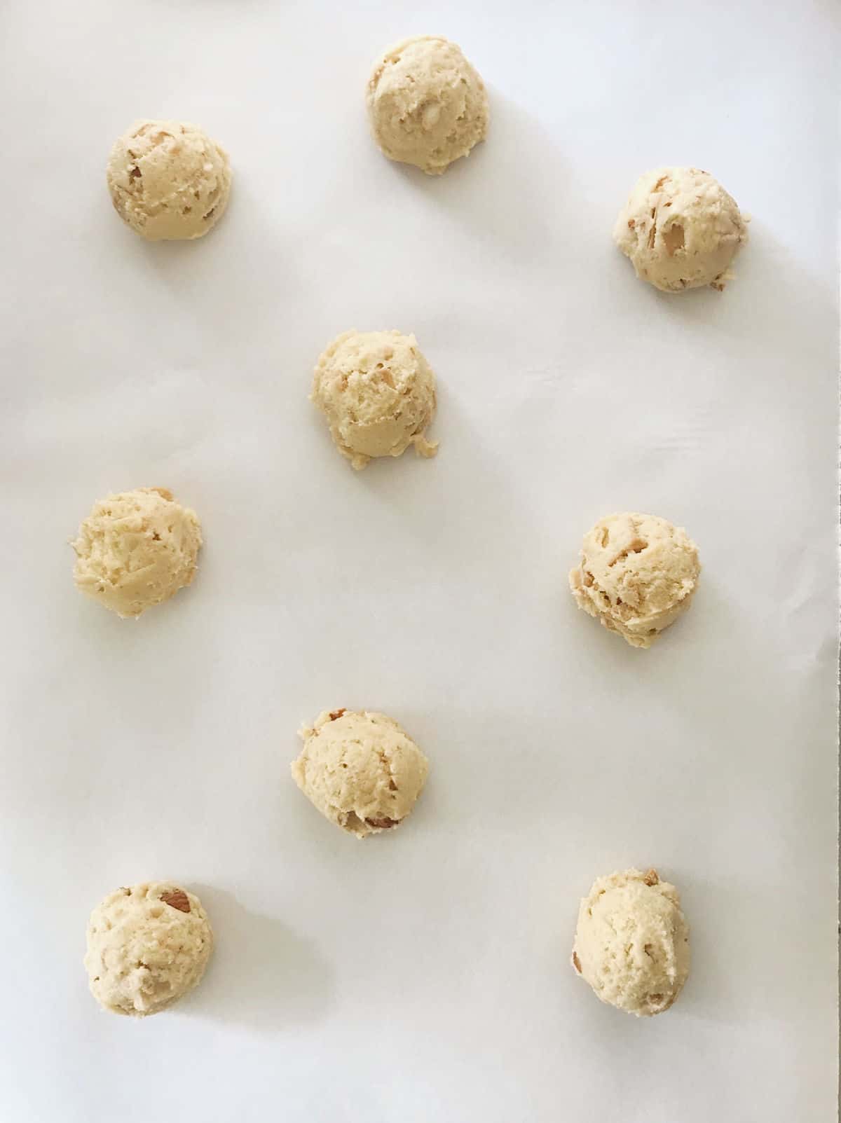 Scoops of unbaked white chocolate almond cookies on parchment paper.