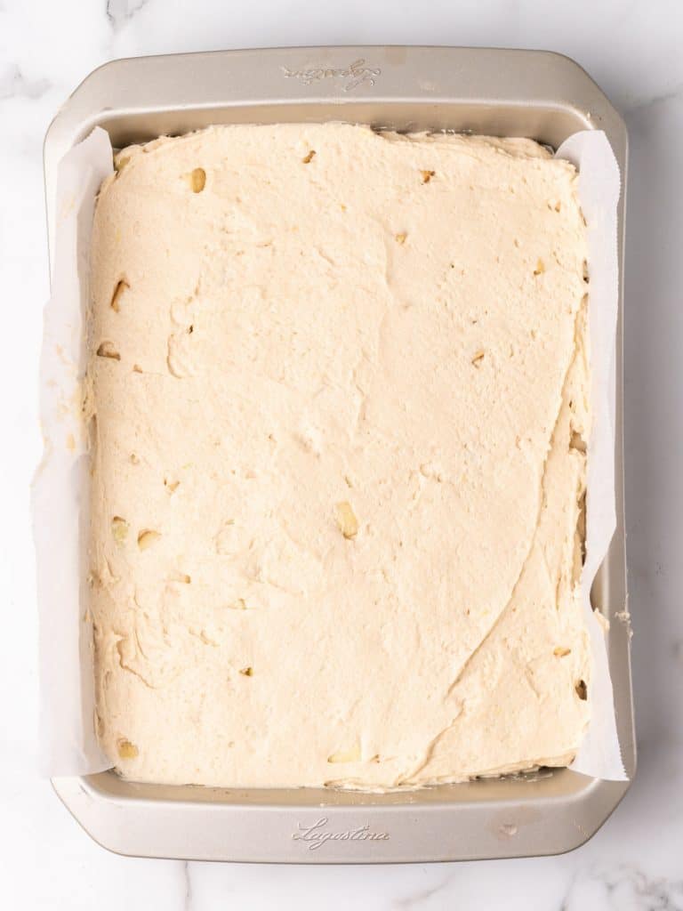 Rectangular metal pan with cinnamon cake batter on a white marble surface.