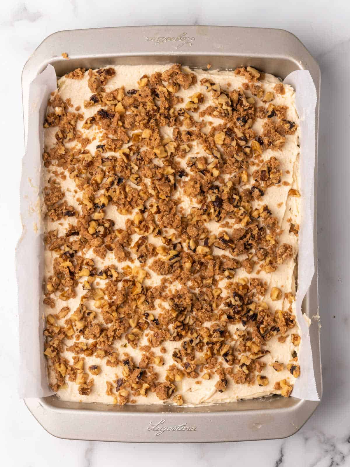 Brown sugar streusel topping on cake batter in a metal rectangular pan on a white marble surface.