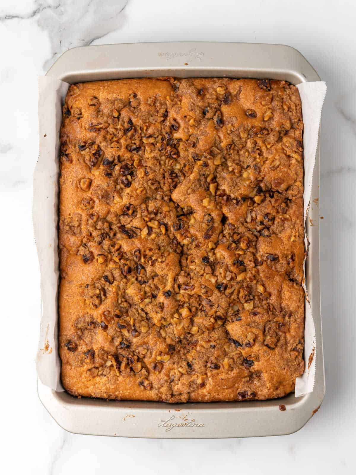 Baked cake with walnut topping on a metal rectangular pan placed on a white marble surface.