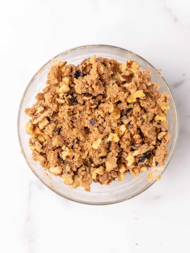 Streusel mixture with walnuts, brown sugar, and cinnamon in a glass bowl on white marble surface.