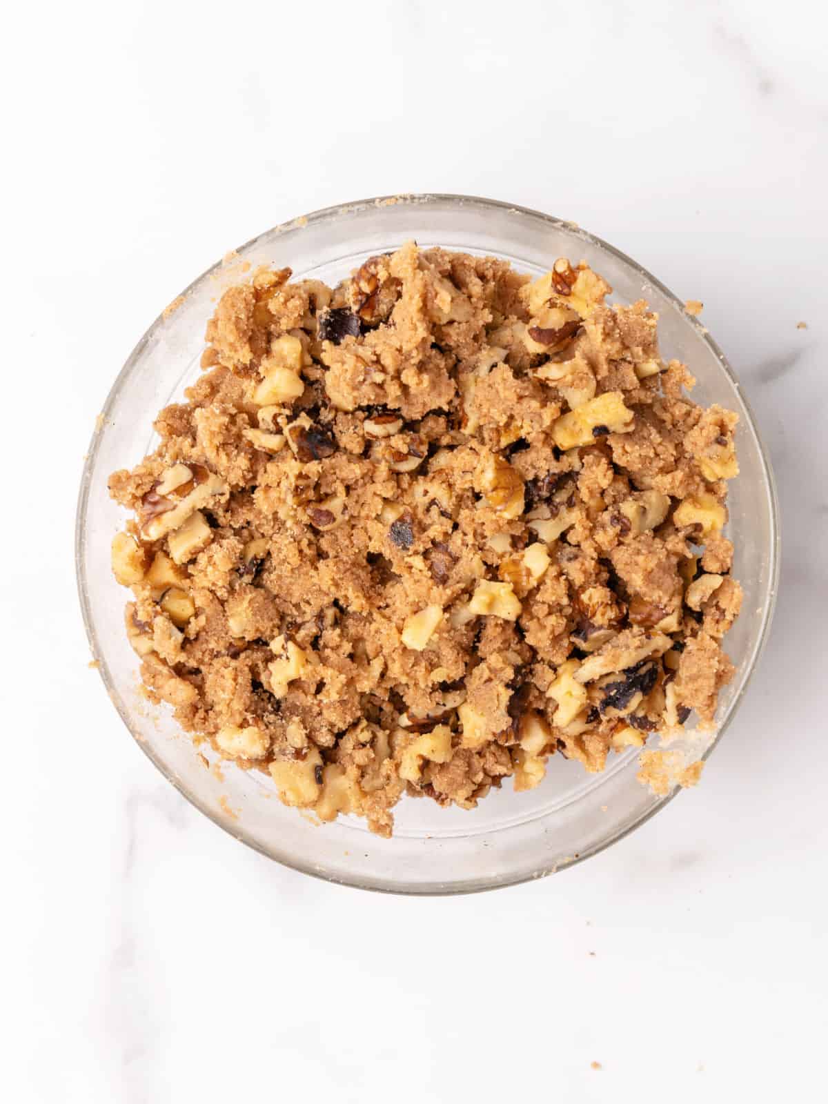 Streusel mixture with walnuts, brown sugar, and cinnamon in a glass bowl on white marble surface.