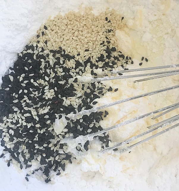 Two types of sesame seeds in bowl with flour, hand whisk