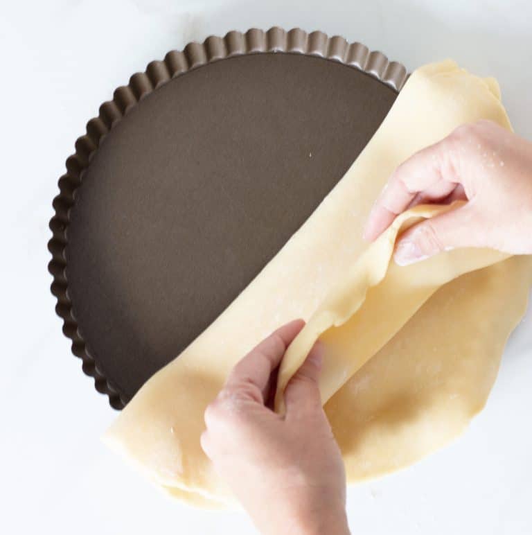 Hands lining metal tart pan with pie crust