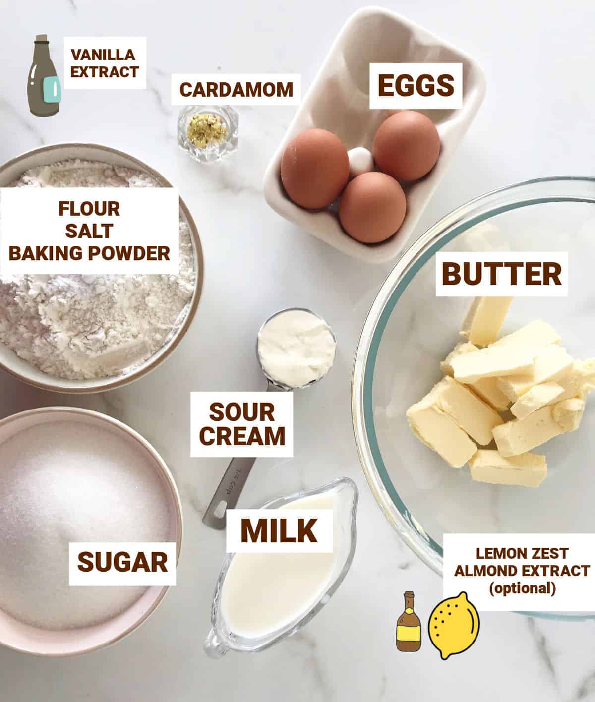 Cardamom cake ingredients in bowls on white surface including eggs, sugar, sour cream, milk, butter, flour