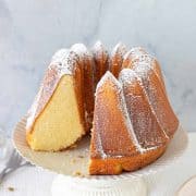 Cardamom Bundt Cake in a white cake stand, one piece missing