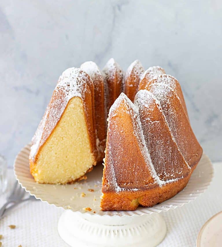 Cardamom Bundt Cake in a white cake stand, one piece missing