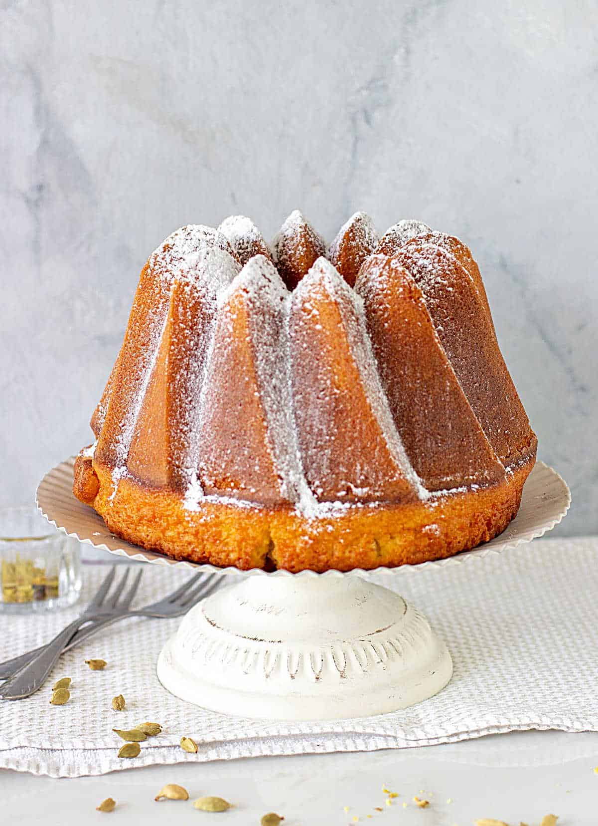 Whole Bundt Cake in a white cake stand, grey background, white surface with napkin