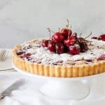 Front view of cherry tart on white cake stand, grey background