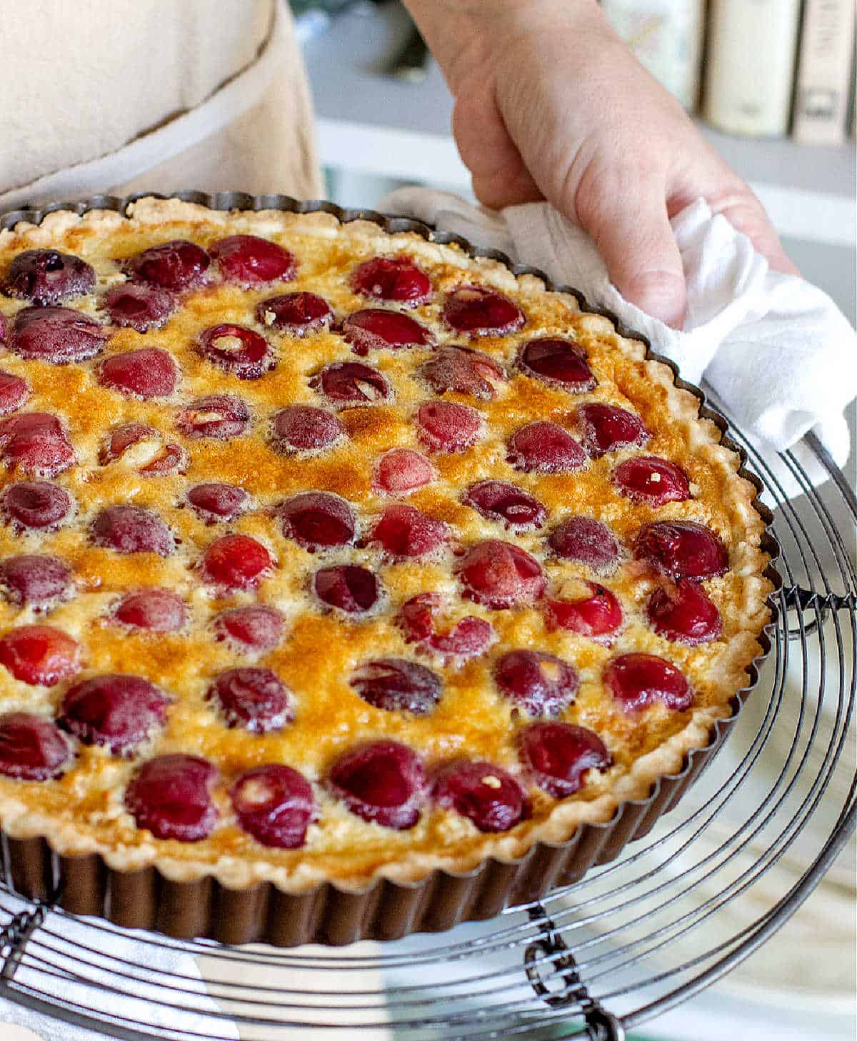 Hands holding baked cherry pie on a wire rack