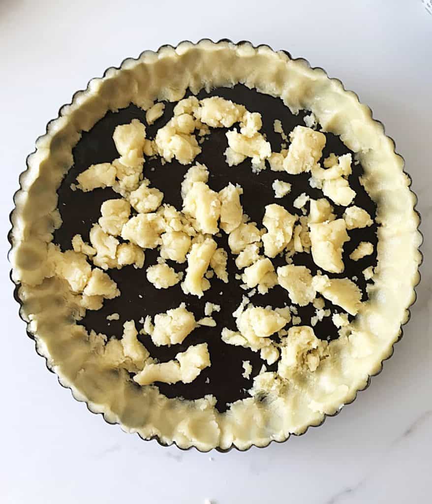Top view of dark pie pan on white marble with half pressed pie crust.