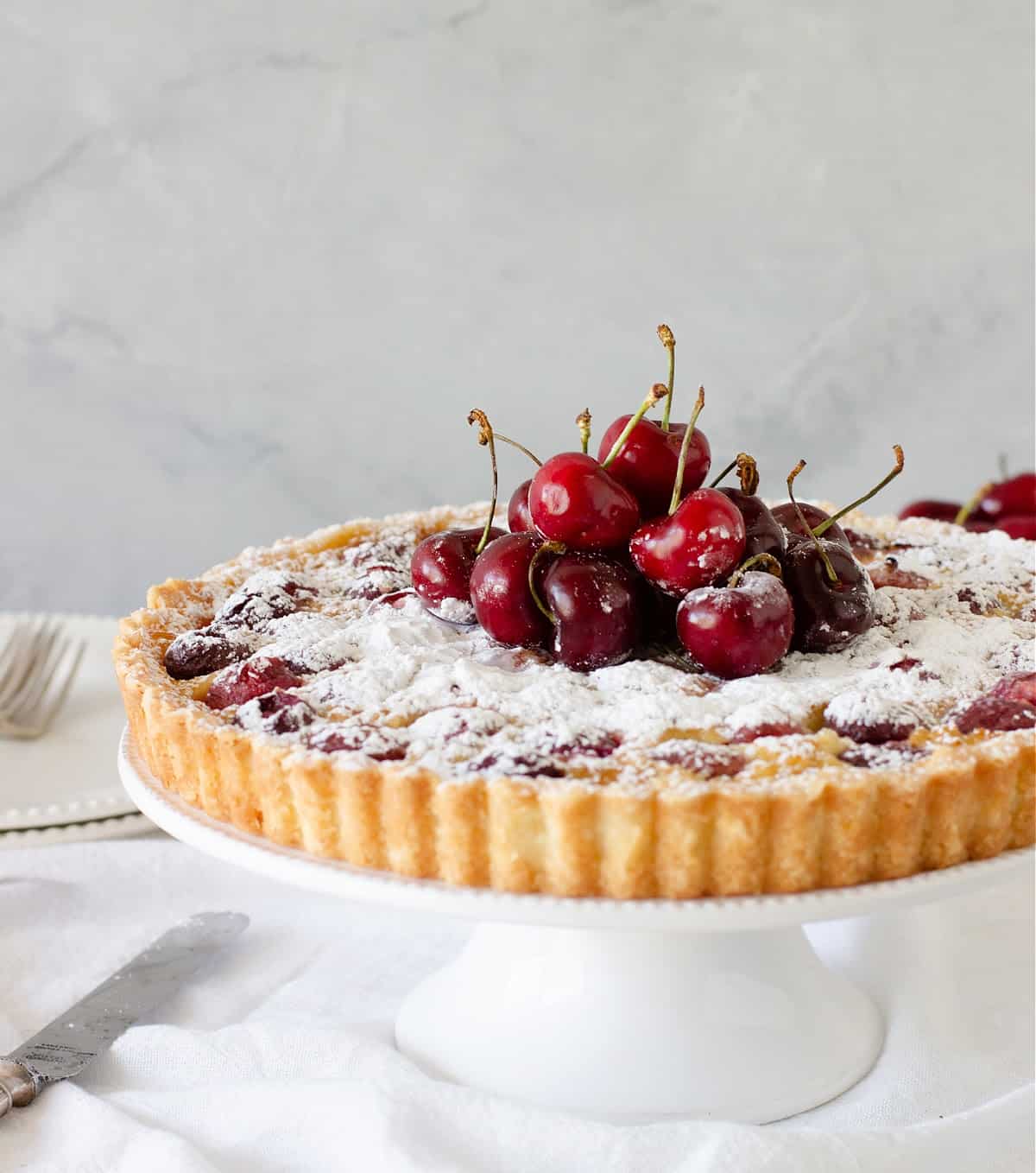 Whole cherry tart on a white pie plate with grey background. 